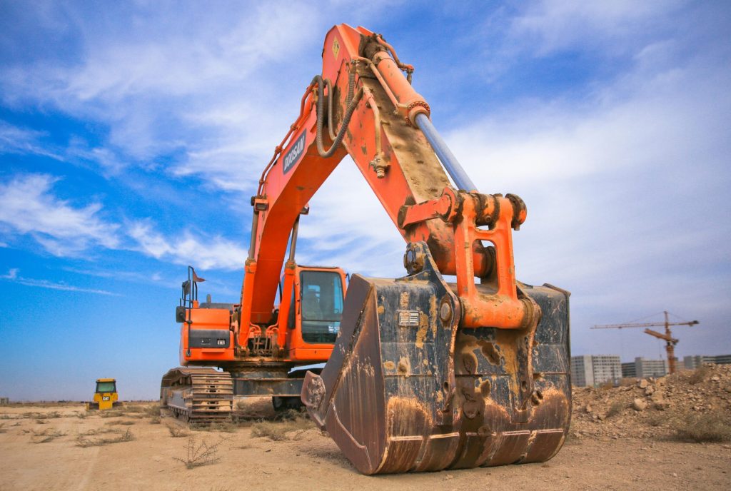 A large orange excavator working on a construction site under a blue sky.